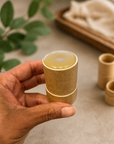 Hand holding a small bamboo cup with tree naturals edge balm on a neutral background