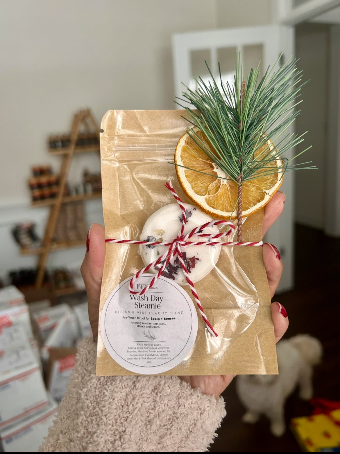 Tree Naturals Wash Day Steamies pouch held in hand in the studio with a small white dog in the background, highlighting everyday self-care.